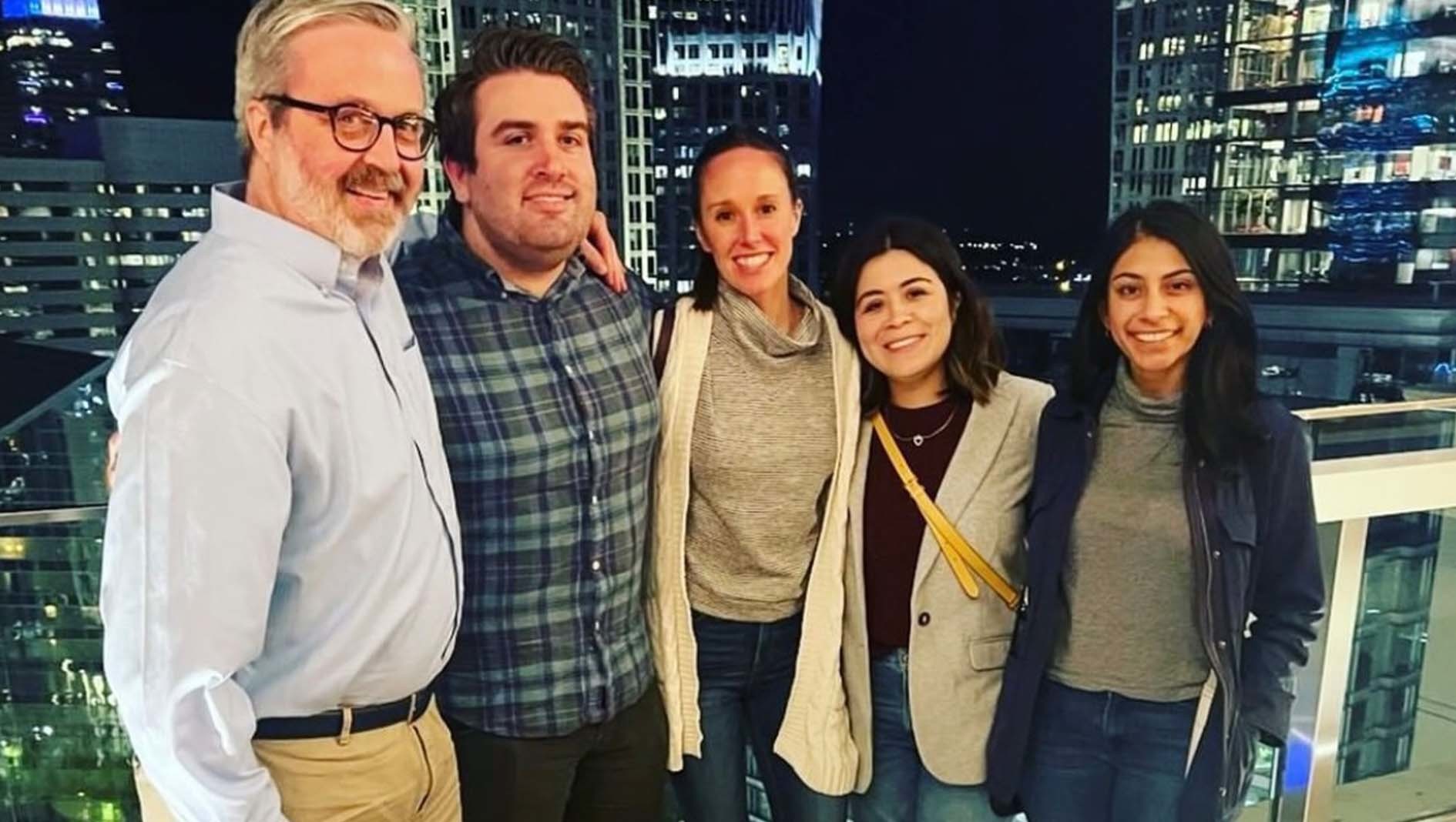 Five members of the Internal Medicine Residency stand together on a balcony for a group portrait. A city skyline is in the background.