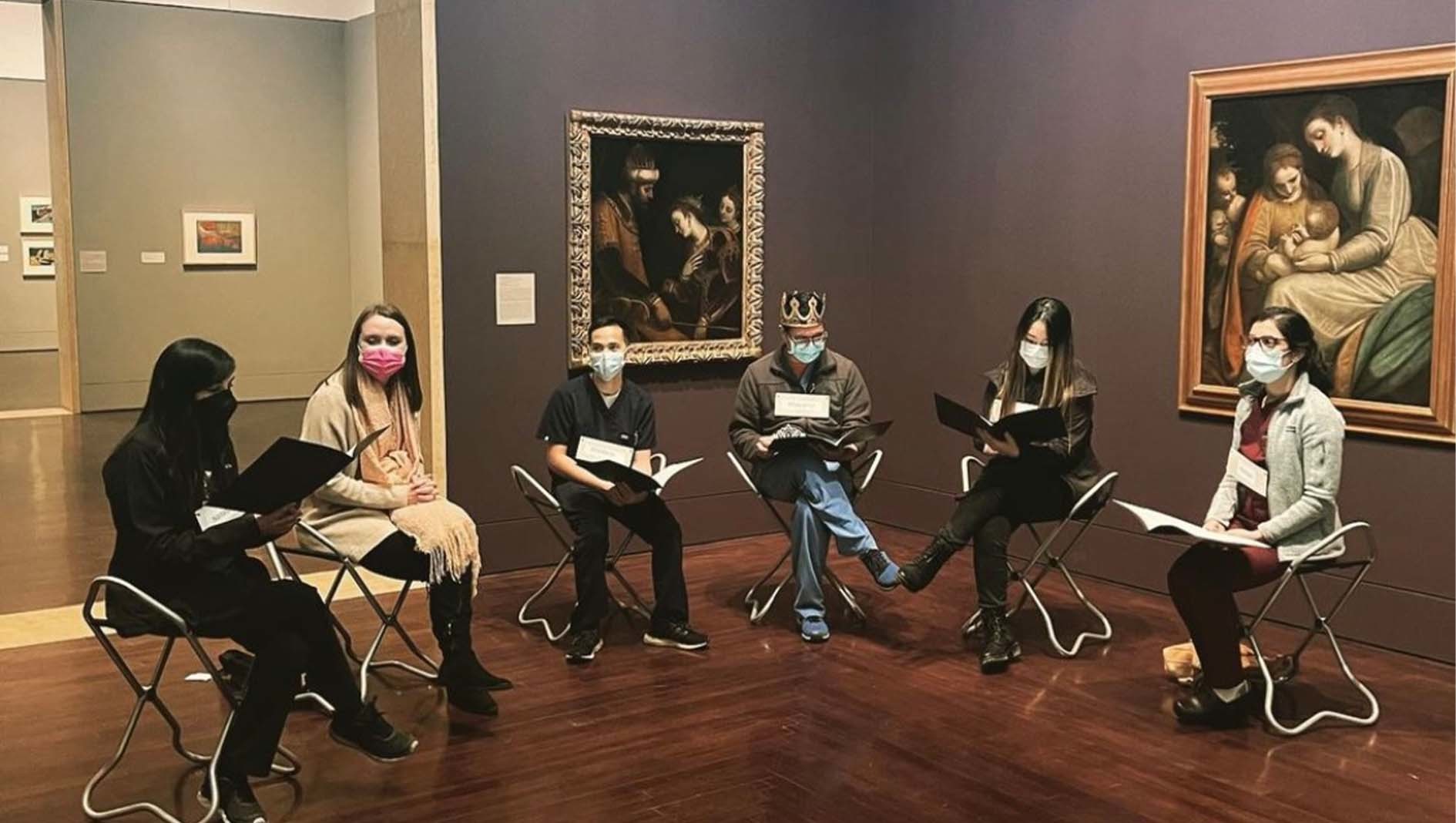 Six internal medicine residents sit in chairs in front of an art exhibit.