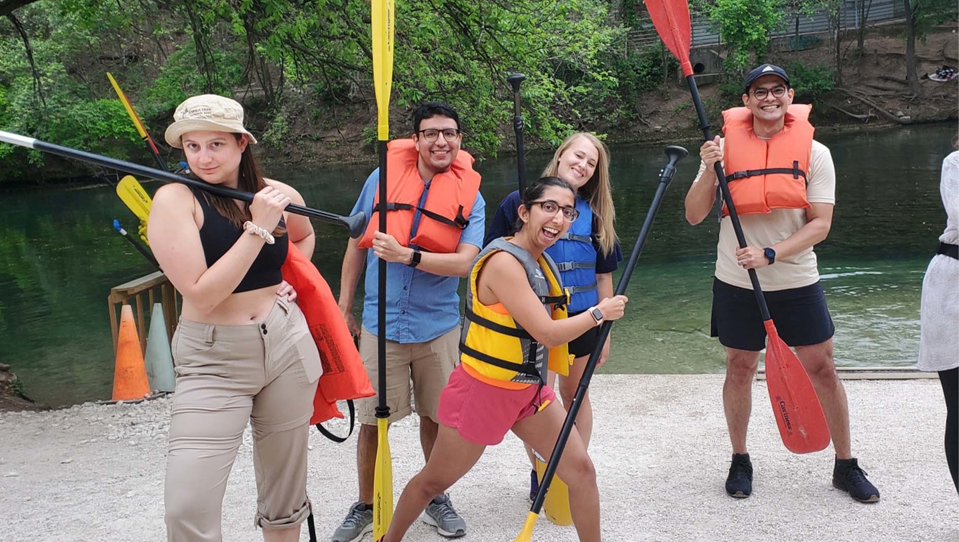 Five internal medicine residents wear flotation vests and hold paddles in a group portrait together.