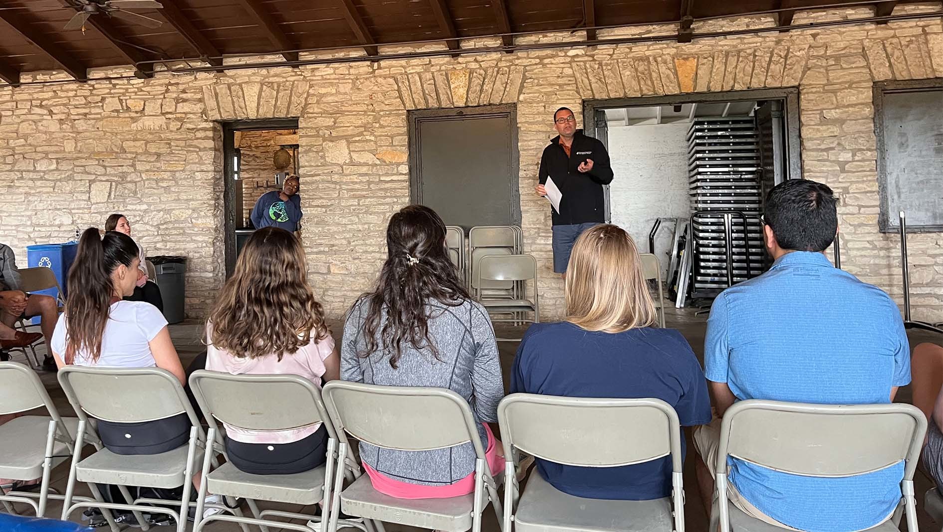 The program director of the Internal Medicine Residency speaks to individuals sitting in chairs outdoors.