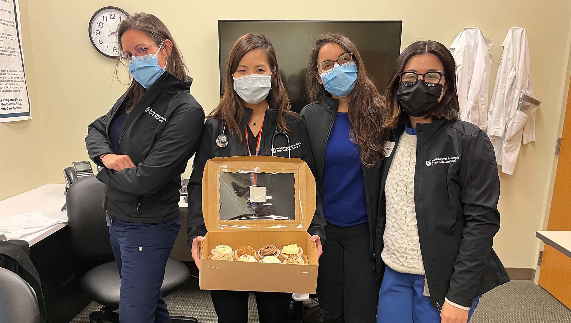 Four internal medicine residents pose together. The resident in the middle of the group holds an open box of pastries.