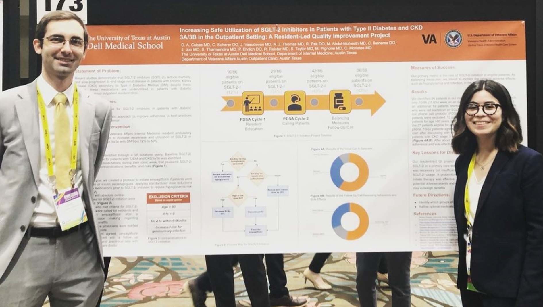 Two internal medicine residents stand in front of a research poster.