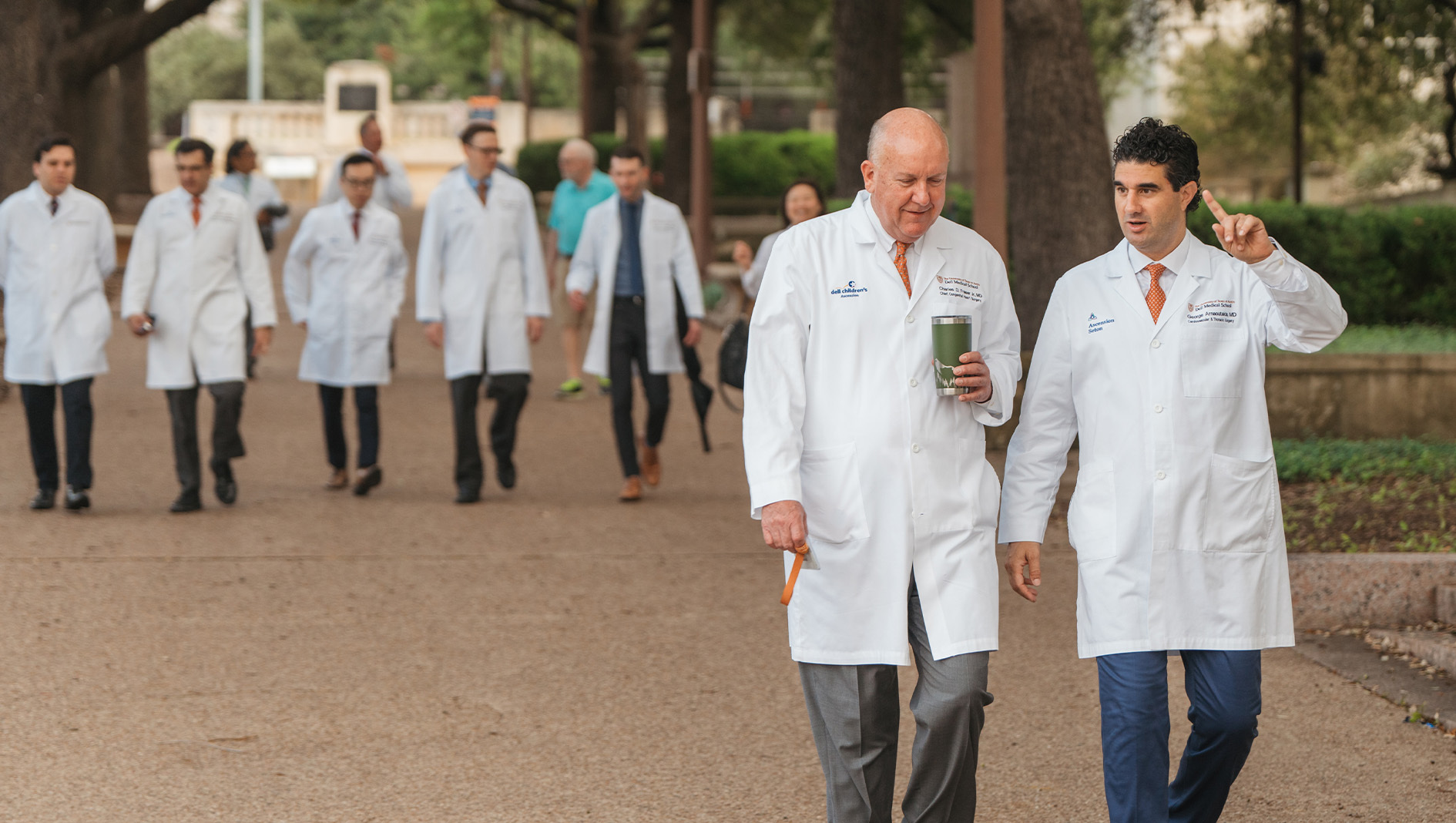 Charles Fraser and George Arnaoutakis walk together outdoors with additional cardiovascular and thoracic surgery faculty members in the background.