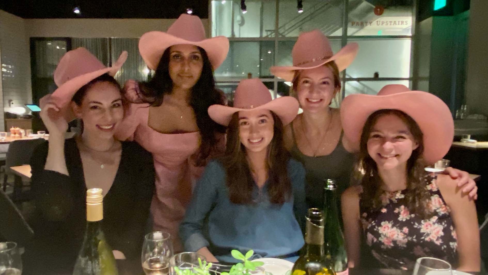 Five members of Dell Med's Transitional Residency together at a dinner table, each wearing pink cowboy hats.