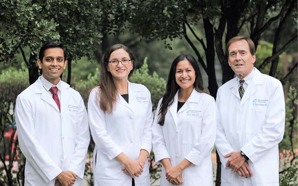 Five members of Eye Associates of Central Texas pose together in a portrait, each wearing their medical white coats.