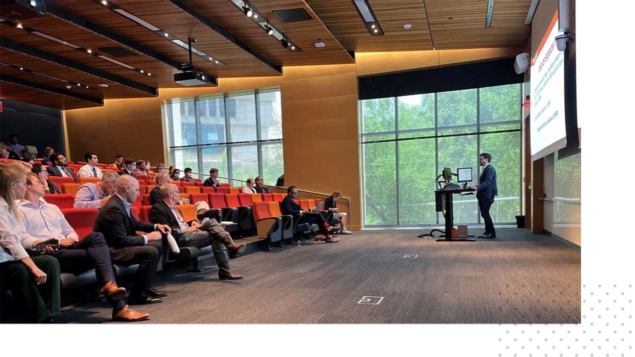 A faculty member presents a slide deck to an audience within a Dell Medical School auditorium.