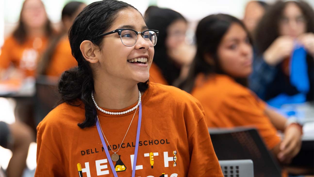 In a classroom and among other student, a younger female student smiles in the direction of an activity.