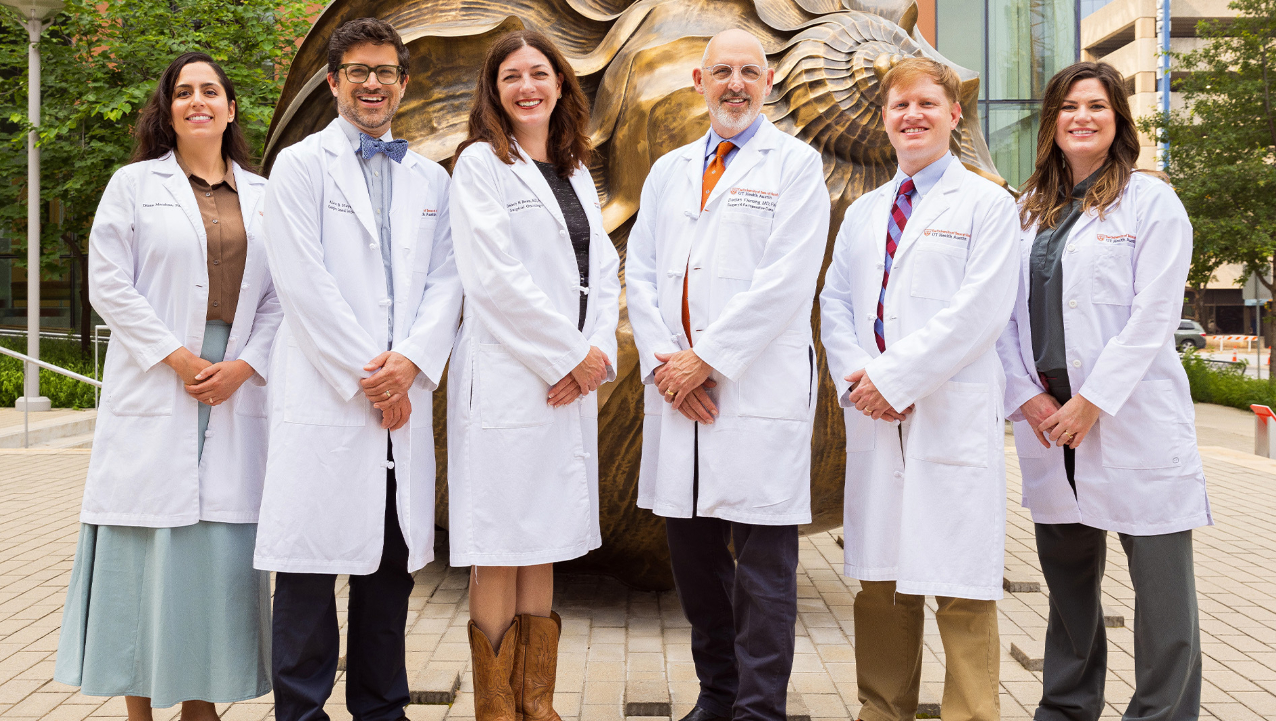 Division of Surgical Oncology faculty members, all wearing medical white coats, stand for a group portrait outside the Dell Medical School campus.