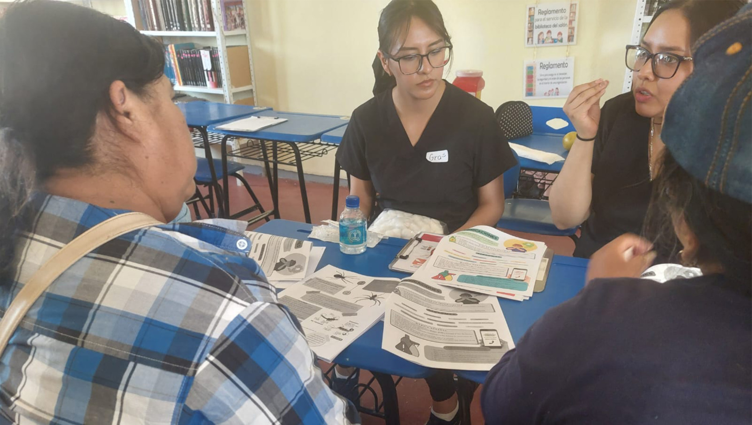 Community health promoters discuss health knowledge with individuals sitting at a table.