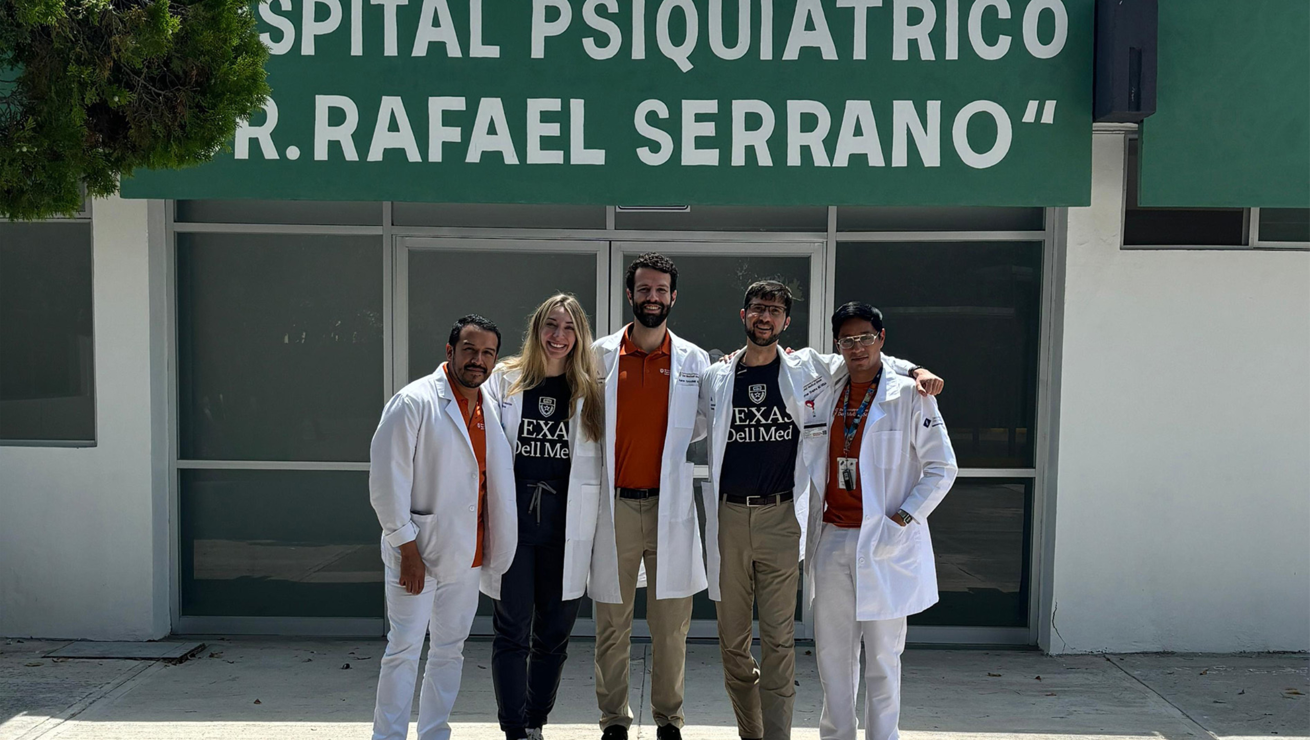 Five Dell Medical School psychiatry residents, all wearing medical white coats, stand in front of a psychiatric hospital in Mexico.