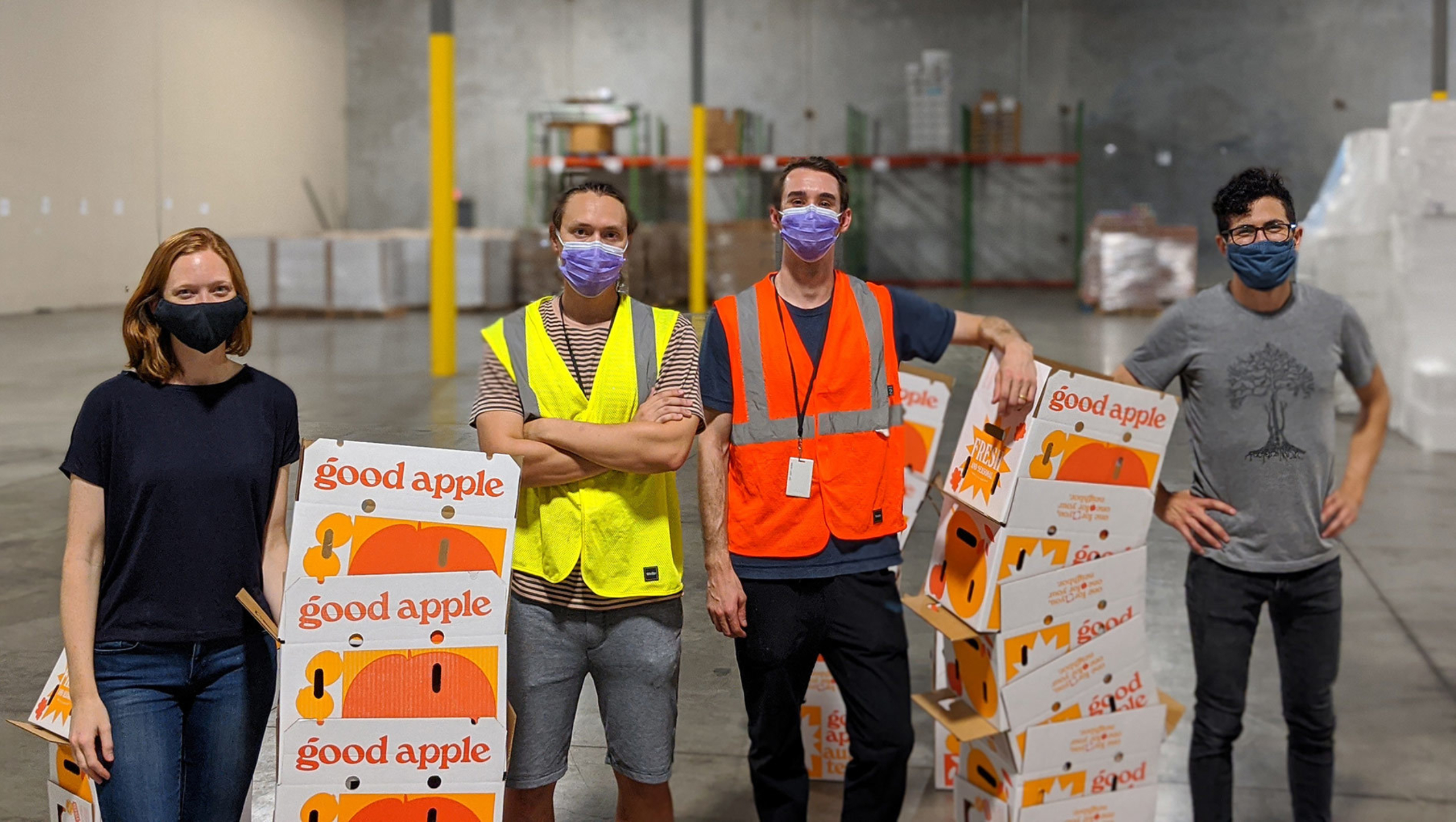 Four members of the Good Apple team standing in a warehouse with produce boxes.
