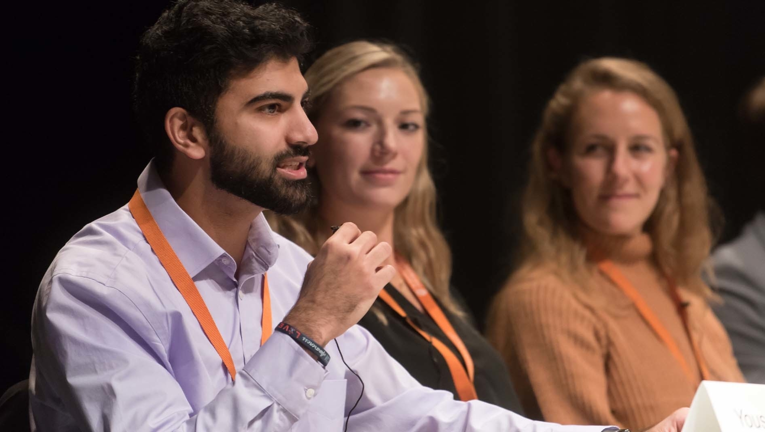 A man on a panel speaks. Two women seated next to him look on.