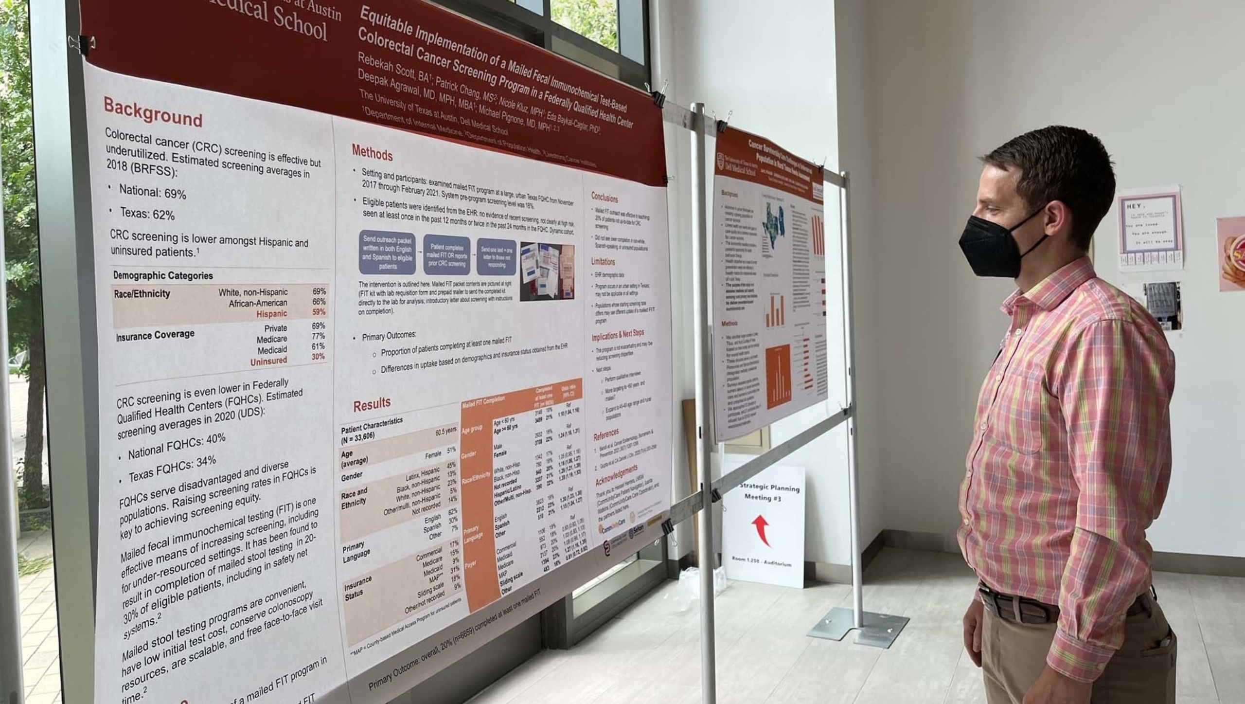 A man wearing a medical mask stands in front of a colorectal cancer research poster.