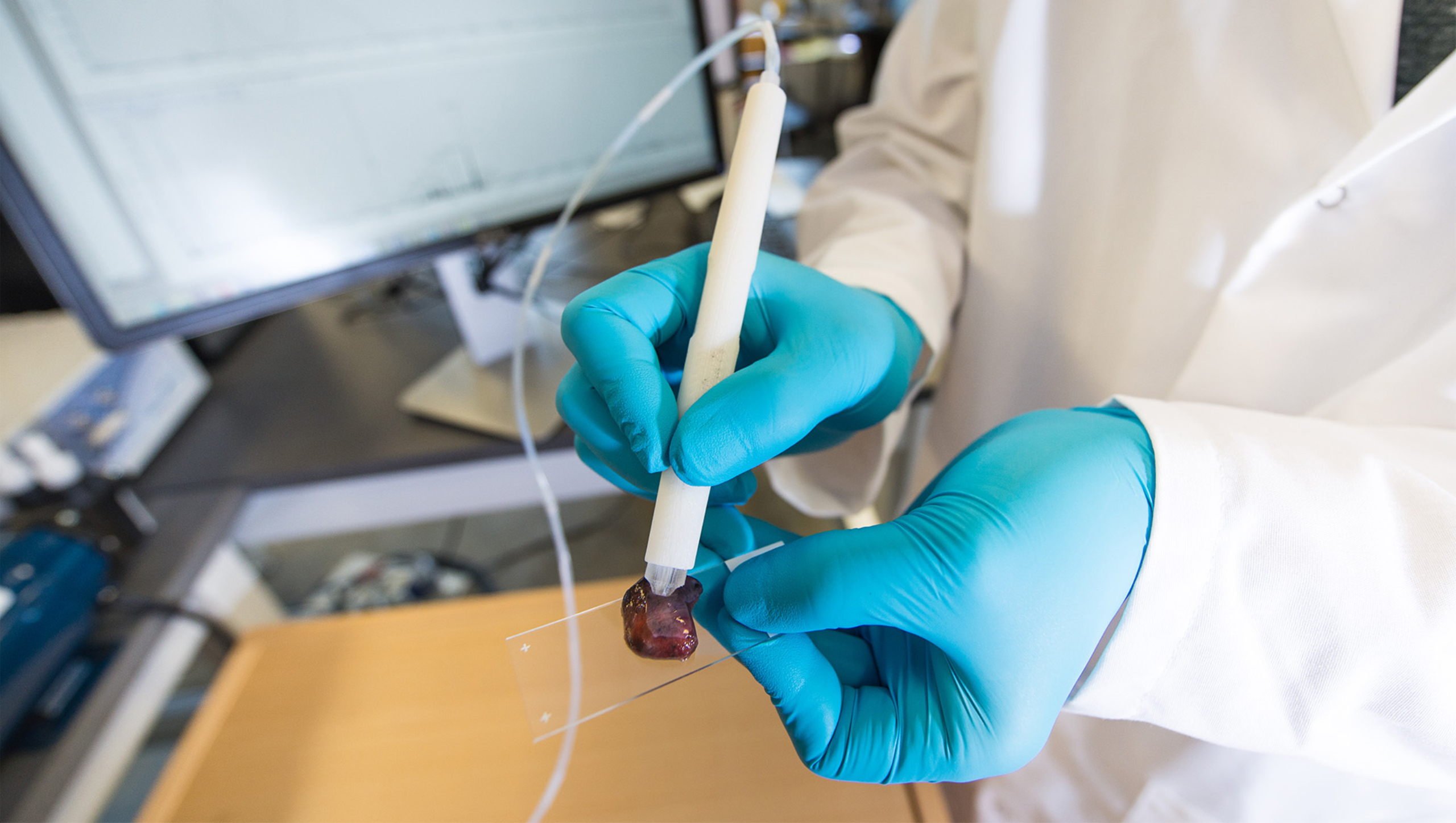 A pair of hands in nitrile gloves interacting with a medical device in the form of a pen.