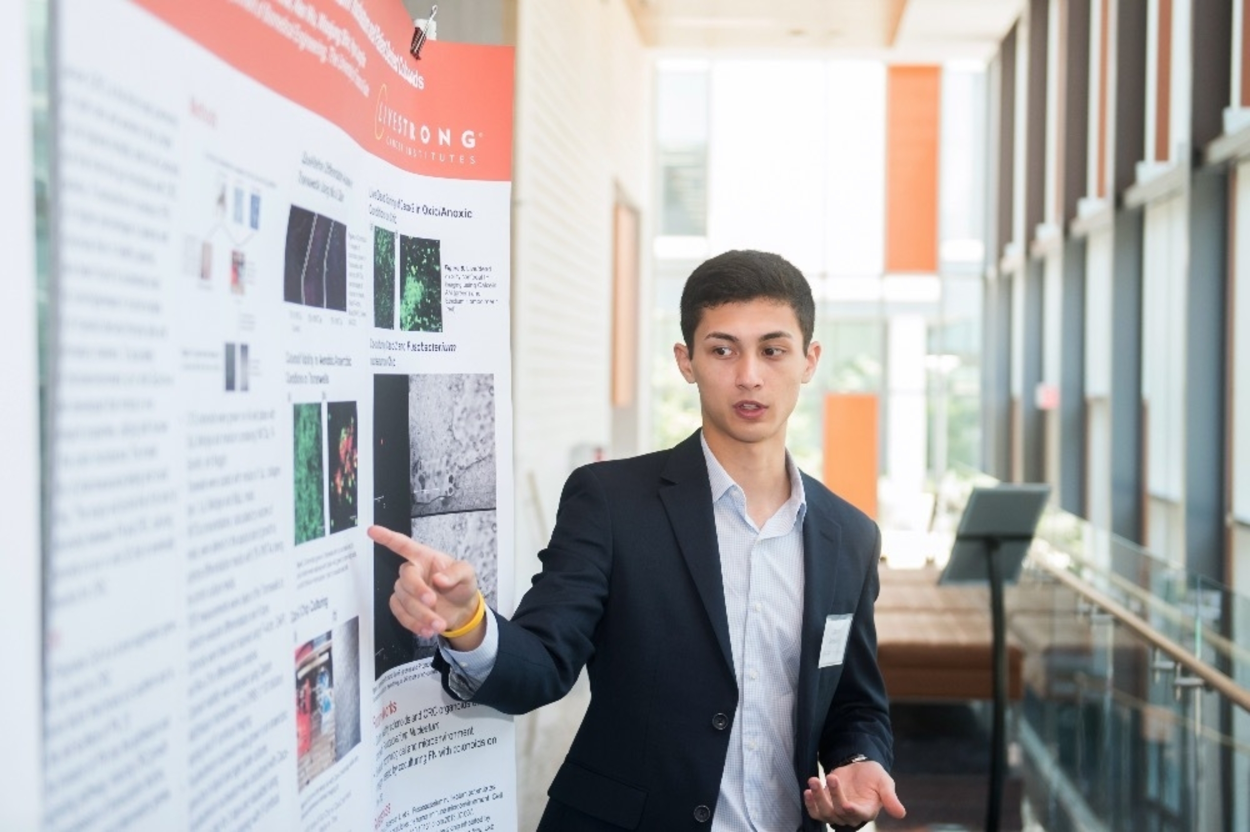 A young male adult presents a research poster at Dell Med as part of a Livestrong Cancer Institutes program.