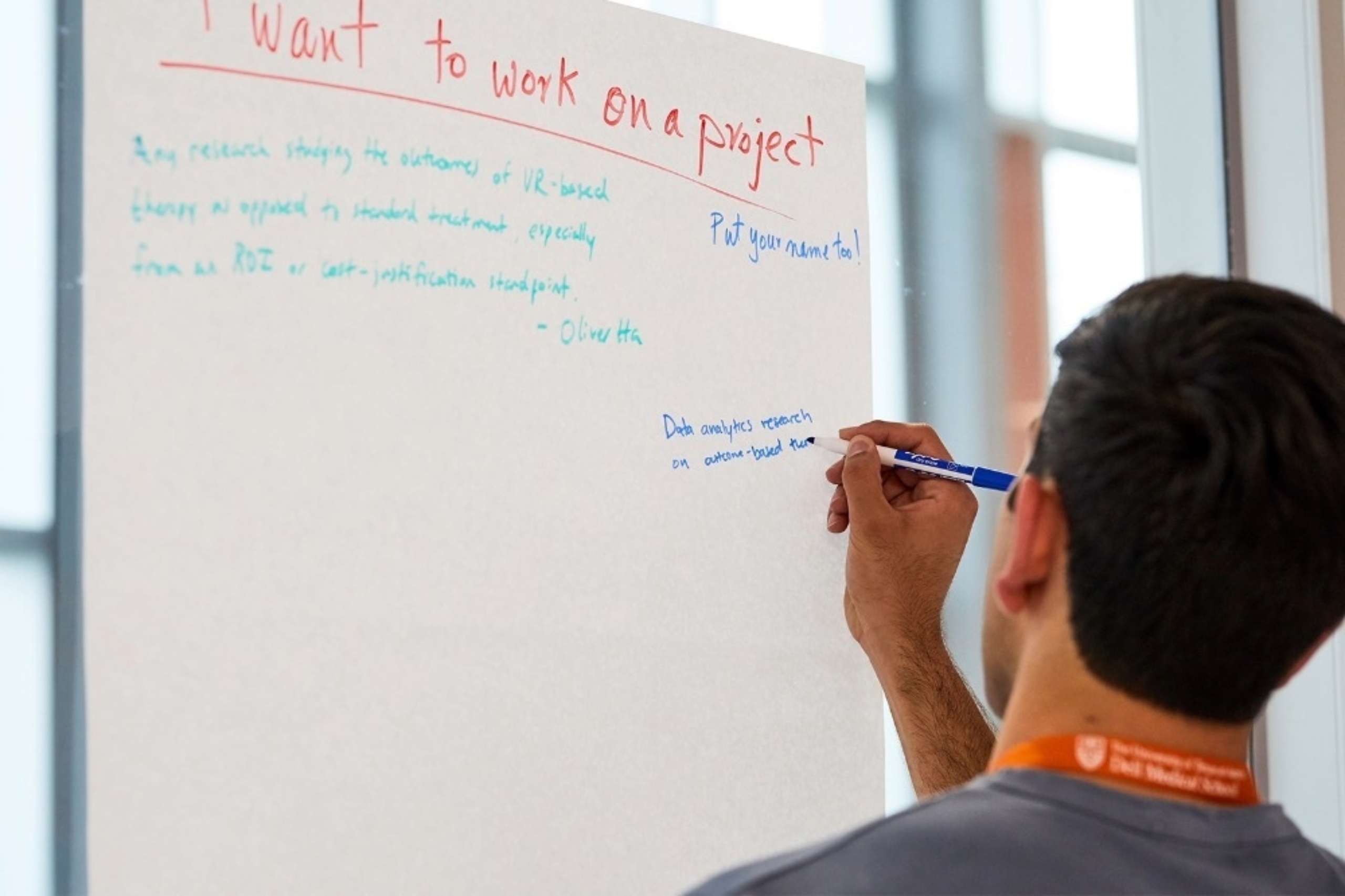 A young male adult writes on a poster as part of an educational activity at Dell Med.