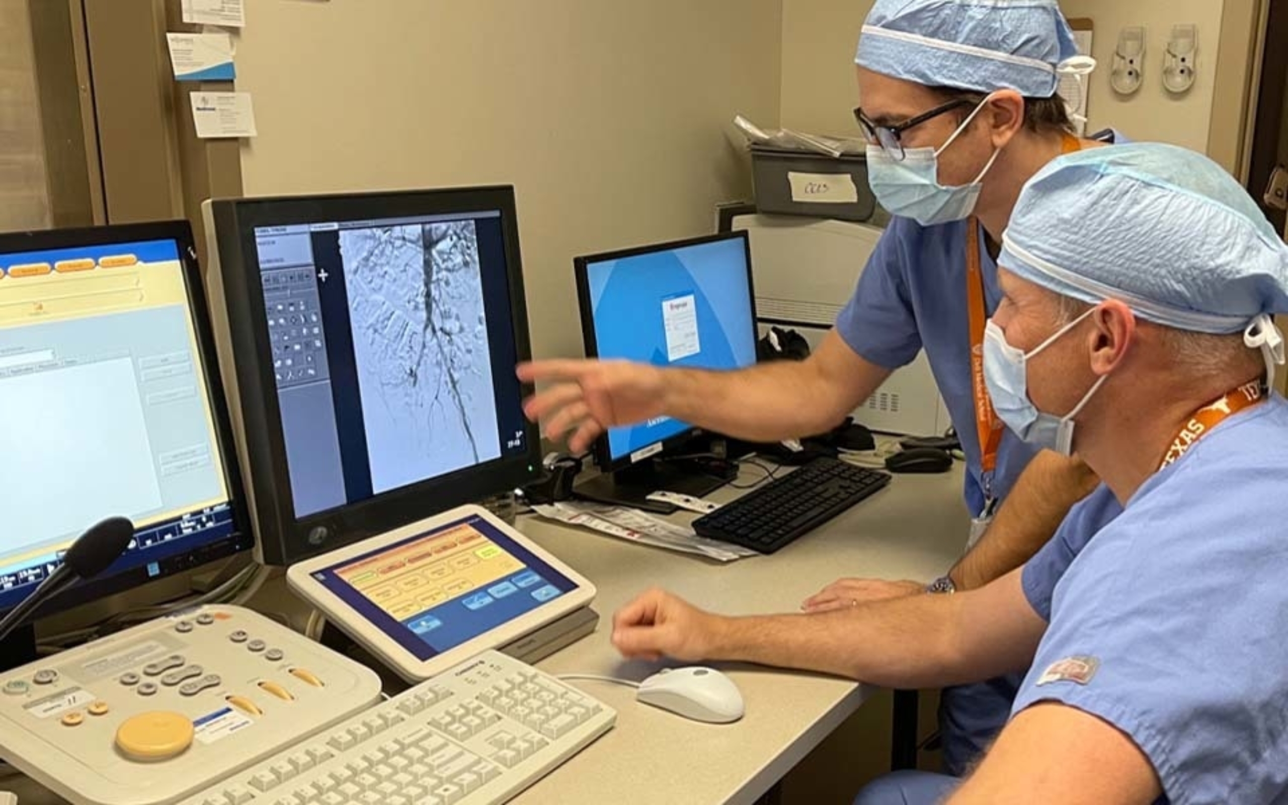 Two male surgeons assess information on a computer monitor.