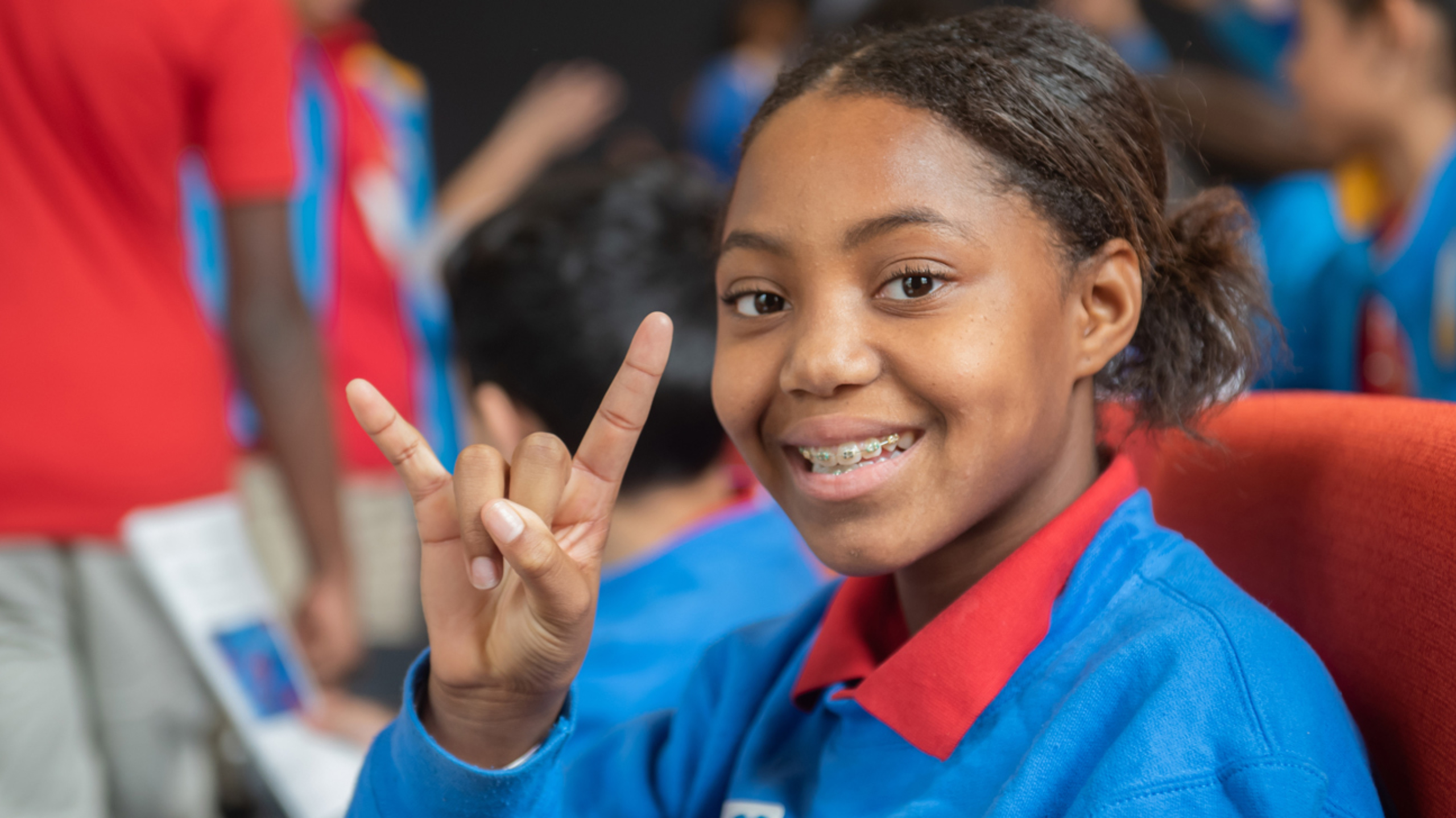 A middle school girl smiling and giving the hook 'em hand sign at the camera.