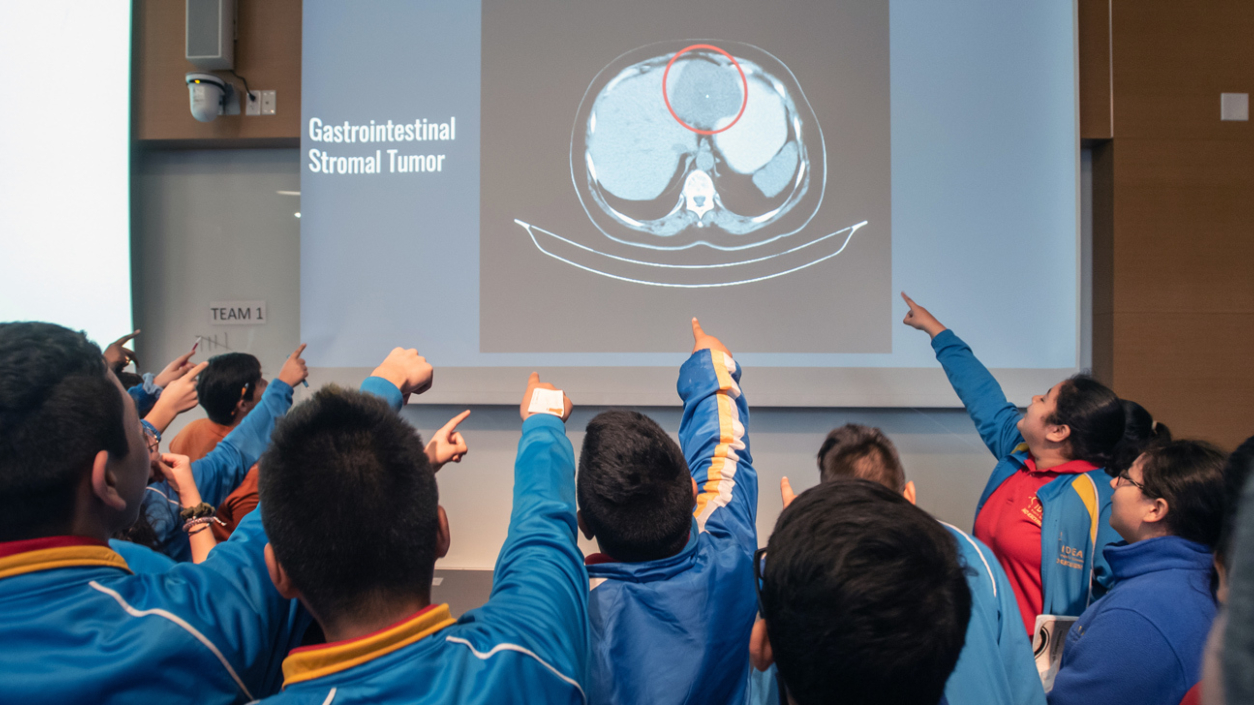 A group of middle school students pointing at a projector screen showing the location of a tumor in a scan.