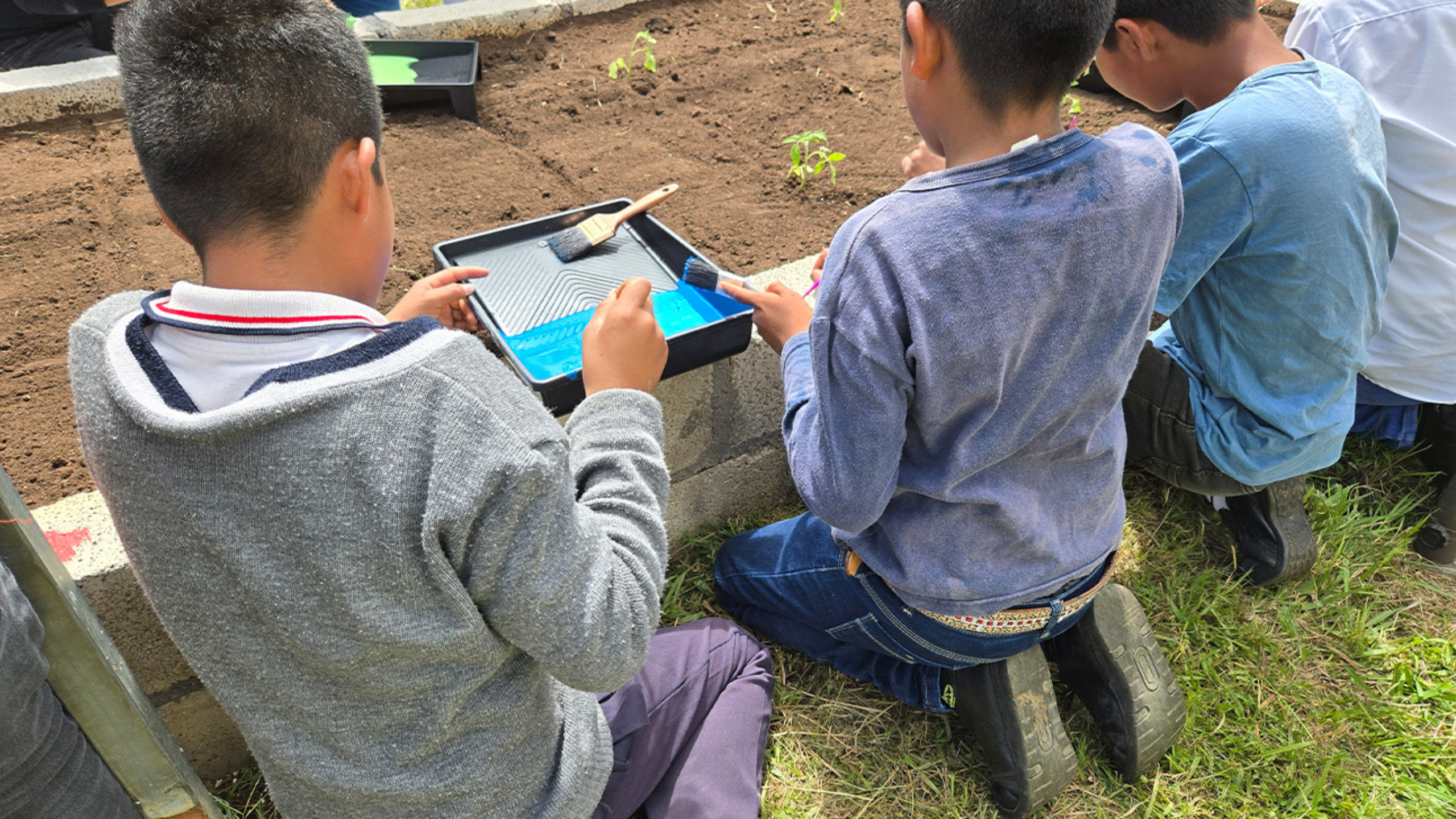 Three boys paint the stone border of a garden.