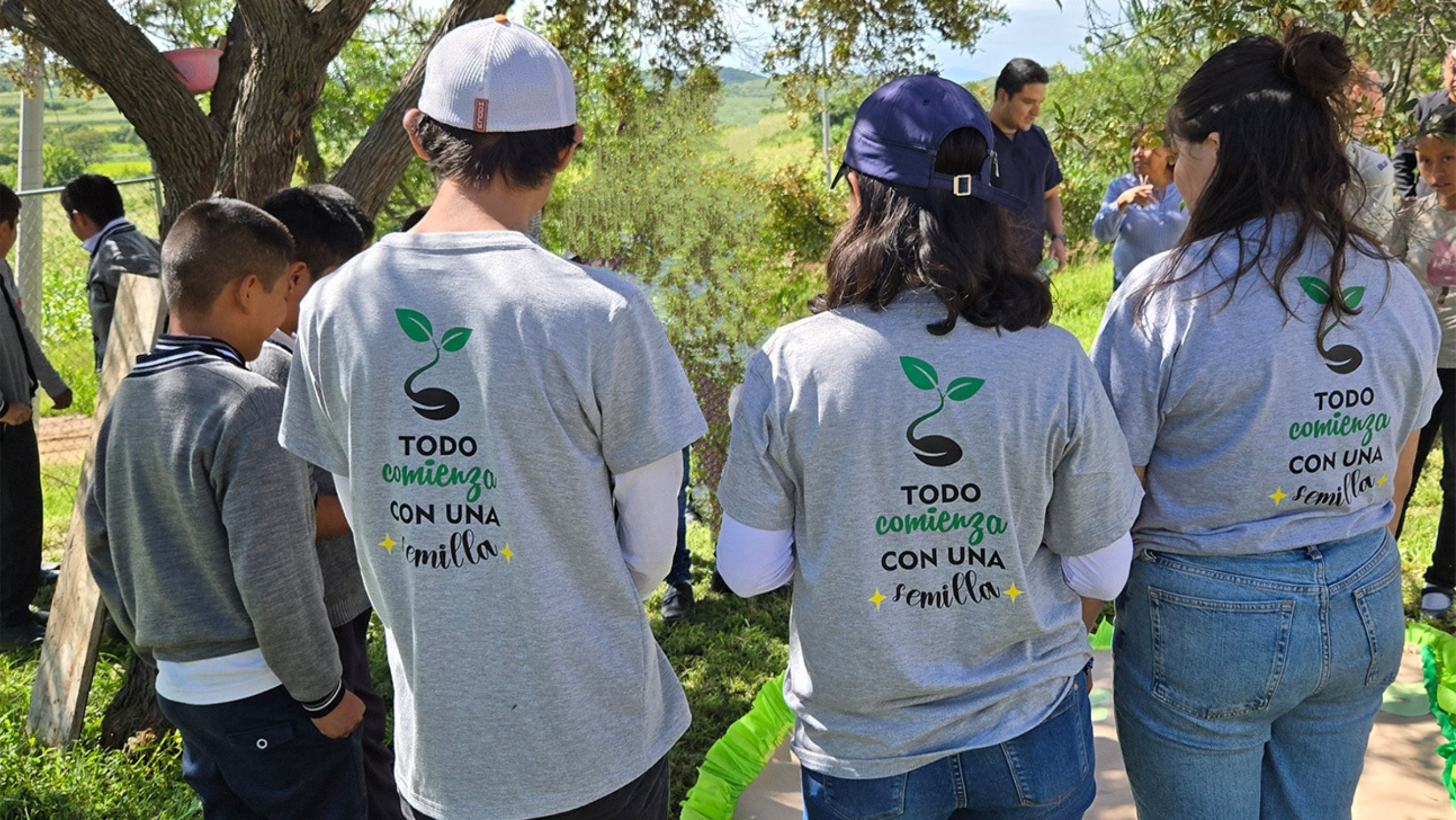 Four people stand together outside with their backs facing the camera.