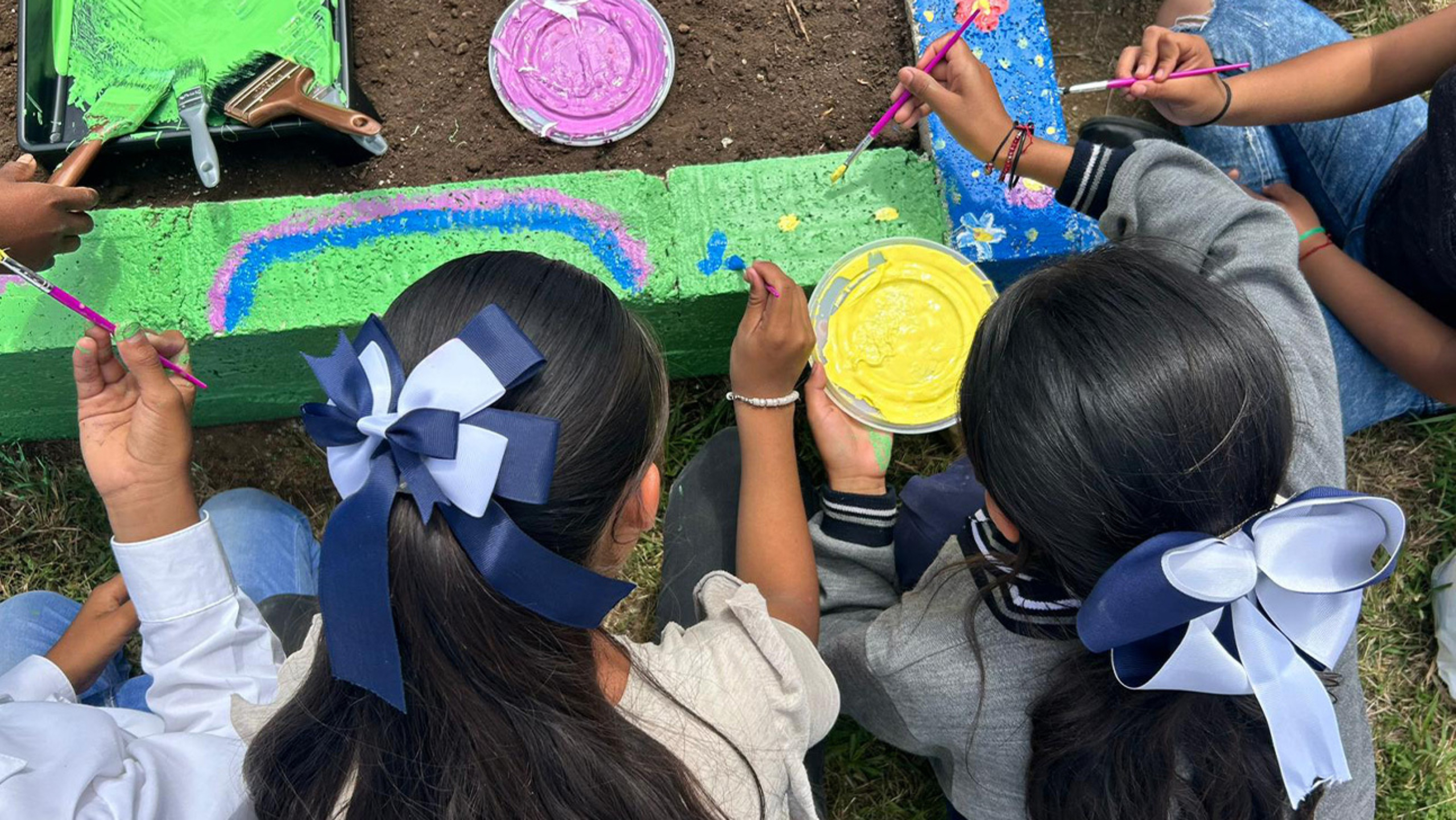 Two girls paint the stone border of a garden.